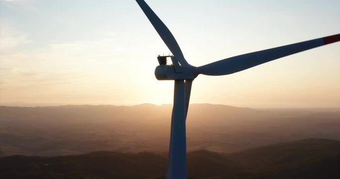 Aerial close up shot of wind mills rotating by the force of the wind and generating renewable energy in a green ecologic way to the planet with a sun shining.