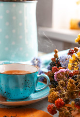 composition still life of a mug with hot leaf tea with berries and autumn leaves on a wooden surface