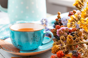 composition still life of a mug with hot leaf tea with berries and autumn leaves on a wooden surface