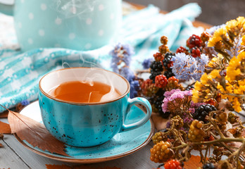 composition still life of a mug with hot leaf tea with berries and autumn leaves on a wooden surface