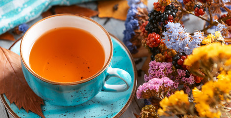 composition still life of a mug with hot leaf tea with berries and autumn leaves on a wooden surface