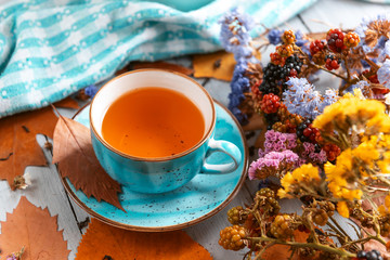 composition still life of a mug with hot leaf tea with berries and autumn leaves on a wooden surface
