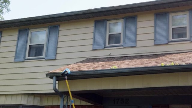 Long pole with scrub brush cleaning the blue exterior gutters and soffit of a house 