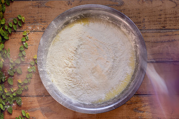 Bowl with ingredients on a wooden surface making a banana bread with flour in the air