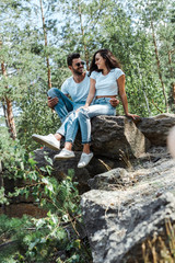 Naklejka na ściany i meble selective focus of man and woman sitting on rocks near trees