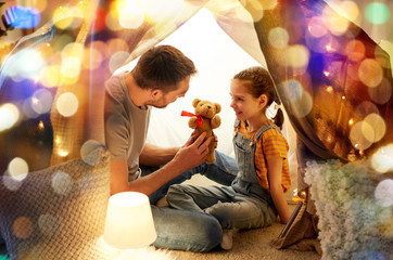 family, hygge and people concept - happy father with teddy bear toy and little daughter playing in...