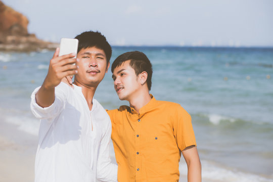 Gay portrait young couple smiling taking a selfie photo together with smart mobile phone at beach, LGBT homosexual lover in the vacation at sea, two man going to travel, holiday concept.