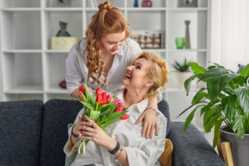Daughter giving flowers to excited mother
