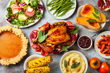 Thanksgiving dinner table with roasted whole chicken or turkey, green beans, mashed potatoes, cranberry sauce and grilled autumn vegetables. Top view, overhead.