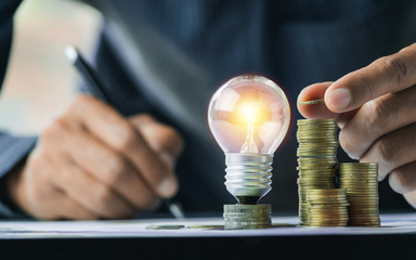 Business man holding light bulb on the desk in office and writing on note book it for...