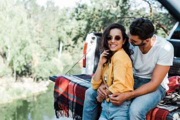 bearded man hugging attractive girl in sunglasses near car