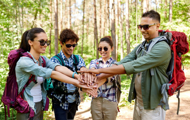 travel, tourism, hike and friendship concept - group of friends with backpacks stacking hands in forest