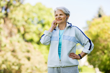 fitness, sport and healthy lifestyle concept - senior woman with earphones at summer park