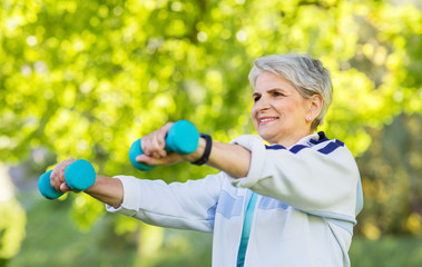 fitness, sport and healthy lifestyle concept - happy smiling senior woman with dumbbells exercising at summer park