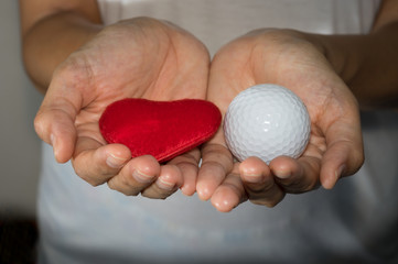 Golf ball and heart in woman hand.
