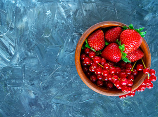 Bowl of red mixed berries on grey background. Berry mix. Delicious fresh ripe red currant and strawberry in a brown bowl, plate, dish. Isolated berry mix with copy space. Space for text. Top view.