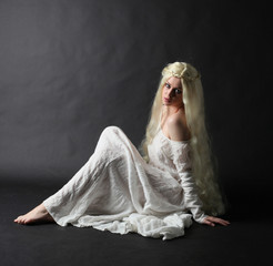 Ghostly full length portrait of a woman with long blonde hair wearing a white robe. Standing pose  against a black studio background.  © faestock