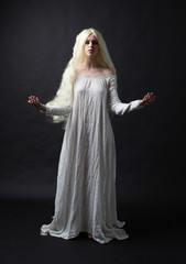 Ghostly full length portrait of a woman with long blonde hair wearing a white robe. Standing pose ...