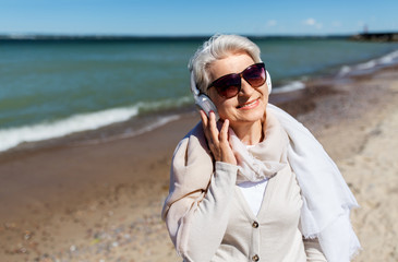 technology, old people and leisure concept - senior woman in headphones and sunglasses listening to...