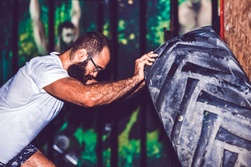 Fototapeta na wymiar Young bearded fitness man moving large tire in the crossfit gym