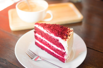 A piece of red velvet cake with coffee cup on table.