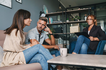 Photo of caucasian focused couple having conversation with psychologist on therapy session in room
