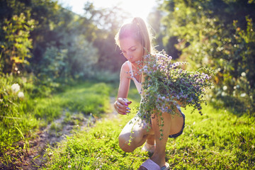 Young woman picking flowers / herbs in nature. © astrosystem