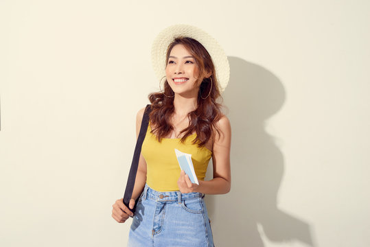 Portrait of young woman wearing trendy outfit, straw hat, travel with backpack  and holding flight ticket, passport