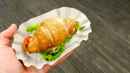 Croissant with avocado, tomato and herbs outdoors. Street vegetarian food