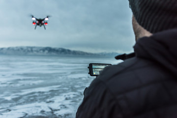 Man flies black drone helicopter over frozen lake
