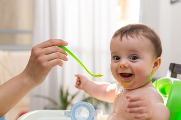 Adorable baby eating food. His mother feeds him with a spoon.