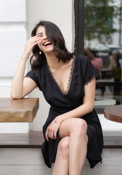 Beautiful elegant brunette girl wearing a black dress with a sexy deep neckline is relaxing in a street cafe. Advertising, fashion, commercial design. Copy space