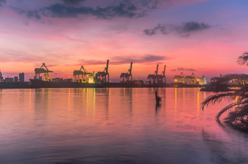 Silhouette container cargo freight ship with working crane bridge in shipyard with sunrise twilight colorful sky for Logistic Import Export background