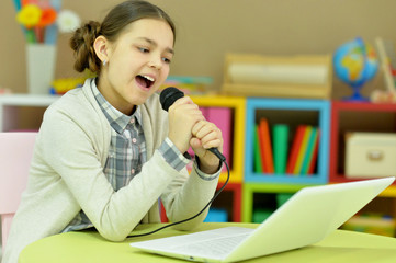 Adorable little girl singing karaoke with modern laptop