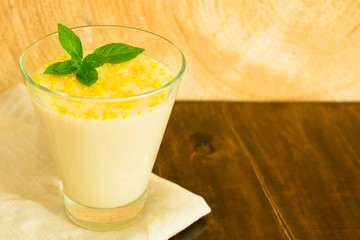 Dessert vanilla pudding with lemon zest and mint in a glass on a wooden table. Copy space.