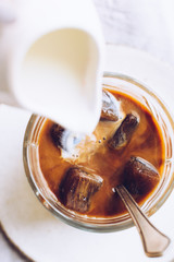 Pouring milk from a jug to a glass of espresso ice cubes