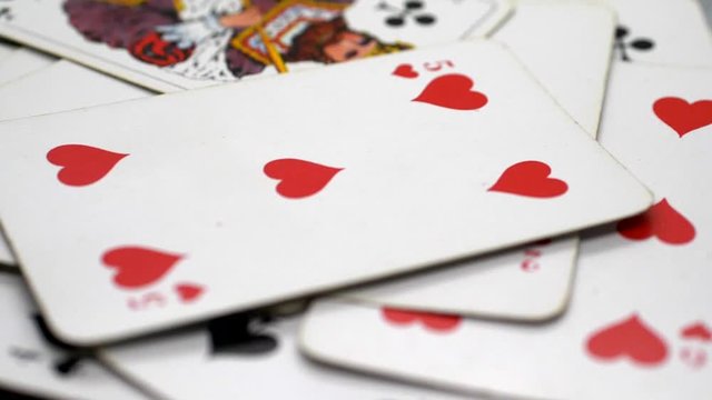Static, closeup shot, of a pack of cards on a moving table, hearts 5 in the middle of the frame