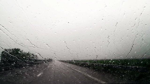 4K footage of rain drops on a moving car windshield.