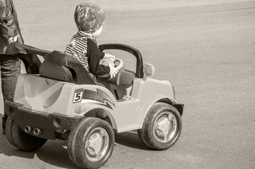 The child is engaged in driving a children's electric car on a flat ground on a warm summer day,...