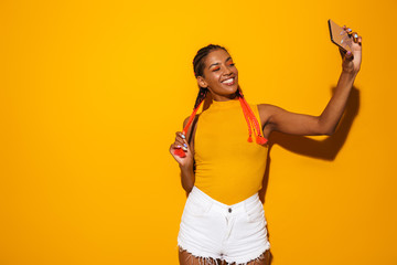 Image of happy african american woman with colorful braids smiling and taking selfie photo on smartphone - obrazy, fototapety, plakaty