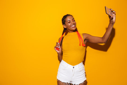 Image of happy african american woman with colorful braids smiling and taking selfie photo on smartphone