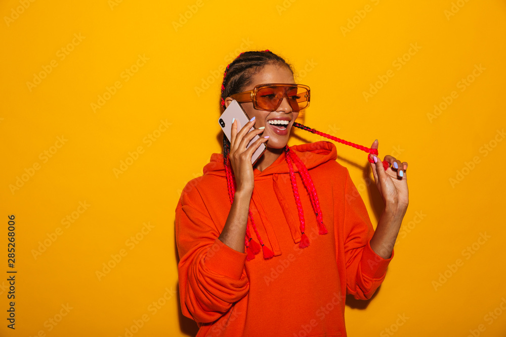 Poster Image closeup of nice african american woman wearing sunglasses and hoodie smiling while talking on cellphone