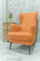 Big orange cotton arm chair and wood cabinet with cement wall background, furniture in living room.
