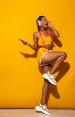 Image of smiling african american woman singing while listening to music with smartphone and headphones