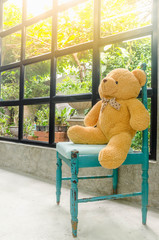 Brown bear sitting on Vintage blue wood chair near checkered glass window for sitting to see garden view.