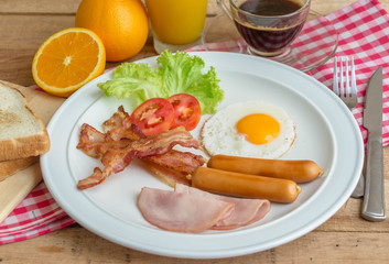 American Breakfast setting with fried eggs, bacon, ham, sausage, and juice.