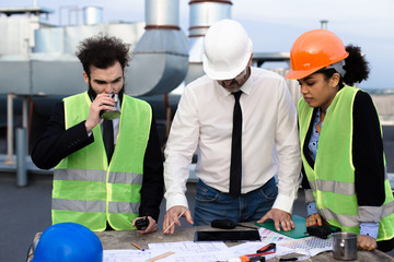 Charismatic young African lady multiethnic group of workers on the top of construction site they chatting with each other analyzing the plan of building wearing the hard hat safety