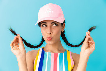 Image of seductive brunette girl wearing summer dress and cap touching her braids