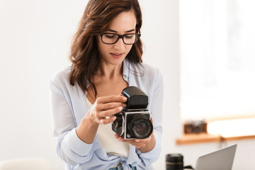 Naklejka premium Amazing young pretty photographer woman in office holding retro old camera.