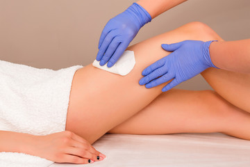 Beautician waxing female legs in spa center. Removing unnecessary hair on the legs. Procedure sugaring in a beauty salon. Sugar depilation. Depilatory sugar paste. Epilation with liquate sugar at legs